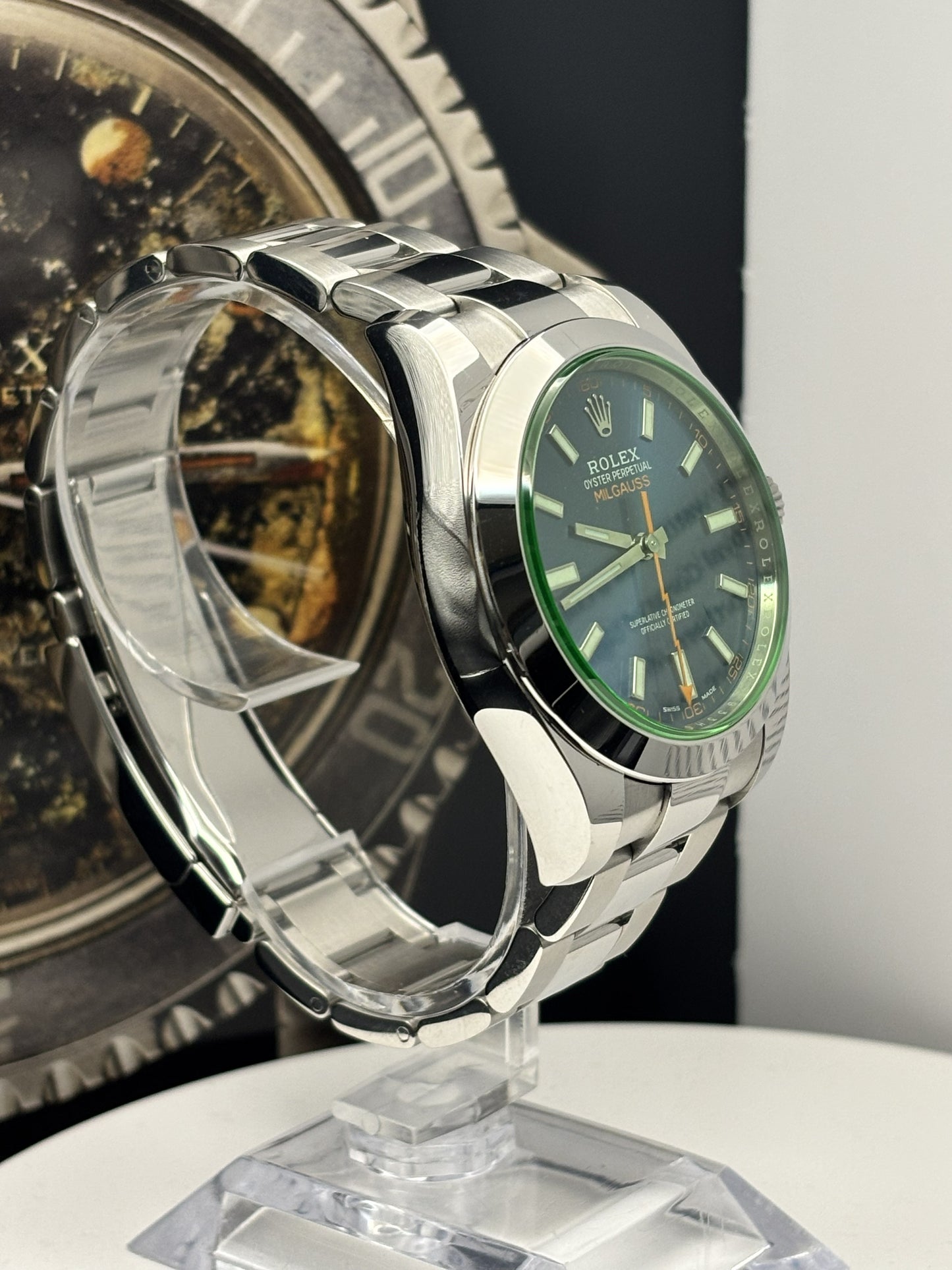 Silver watch with green face on a stand, blurred background