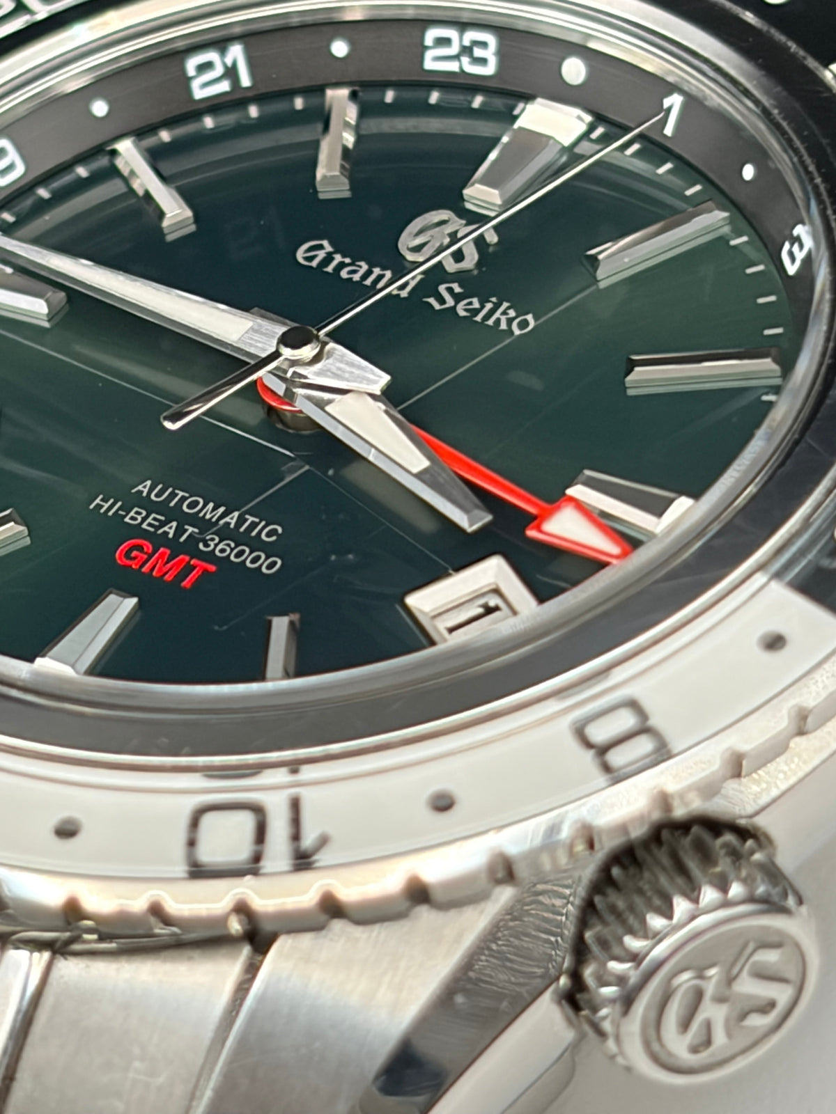 Close-up of a Grand Seiko Automatic Hi-Beat 36000 GMT watch with a dark green dial, silver-tone stainless steel bezel and case, and red GMT indicator accents.