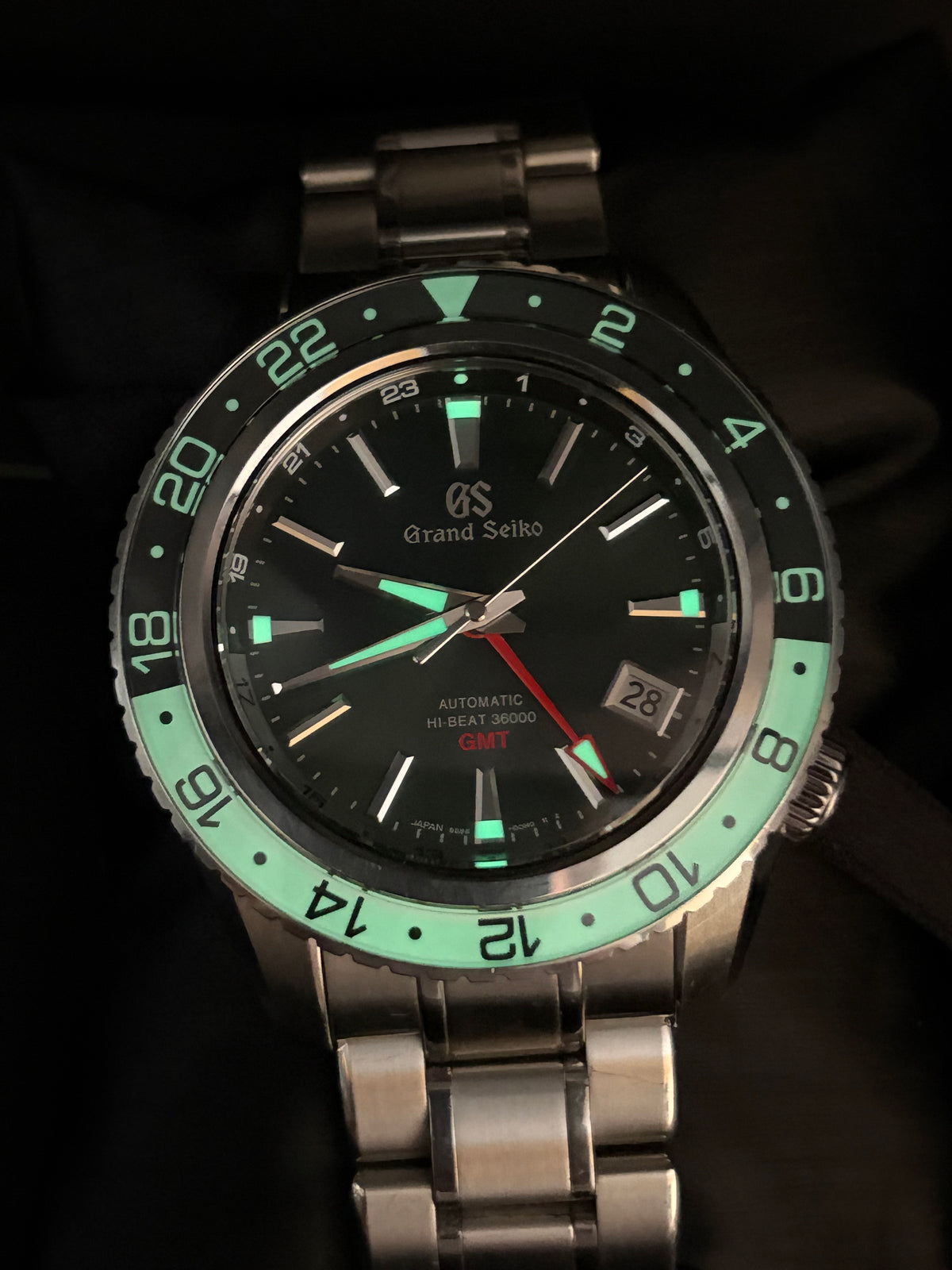 A Grand Seiko dive watch with a black dial, luminous green bezel and markers, and a silver stainless steel bracelet, photographed against a dark background.