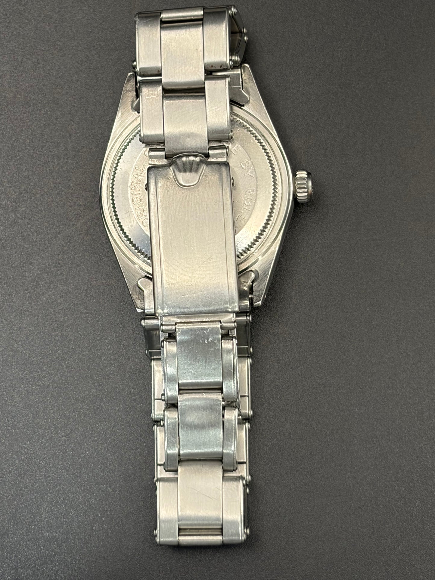 The back of a stainless steel wristwatch with a metal link bracelet, photographed from above on a dark gray background.
