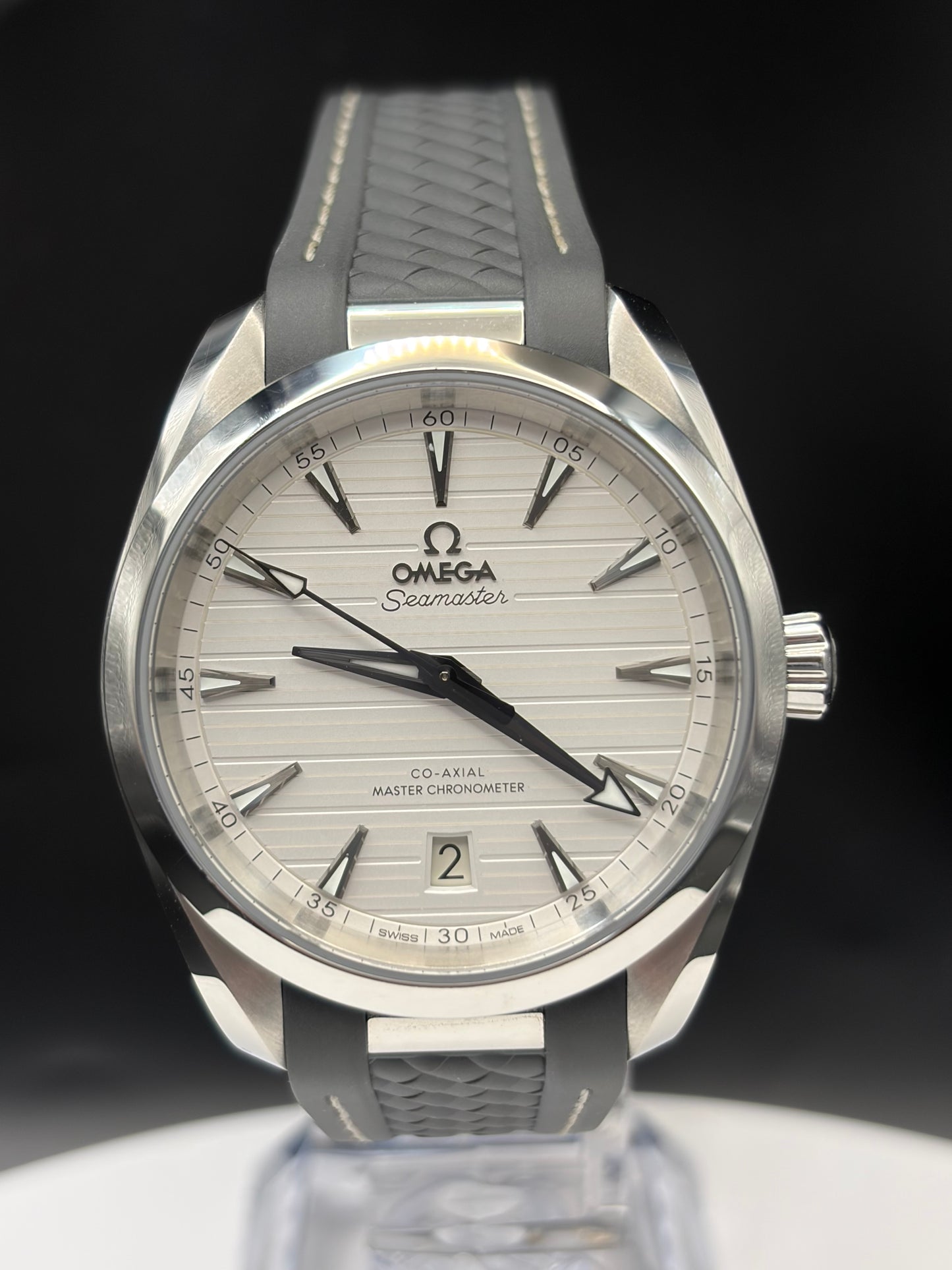 Omega Seamaster Co-Axial Master Chronometer watch with a silver stainless steel case, white sunburst dial, and a gray textured rubber strap, displayed on a clear stand against a black background.