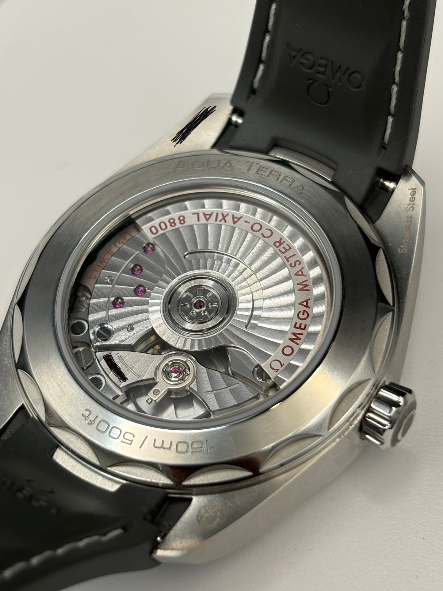 Close-up of the back of an Omega Terra watch with a silver stainless steel case and a black leather strap, showing the detailed automatic movement through a transparent case back.