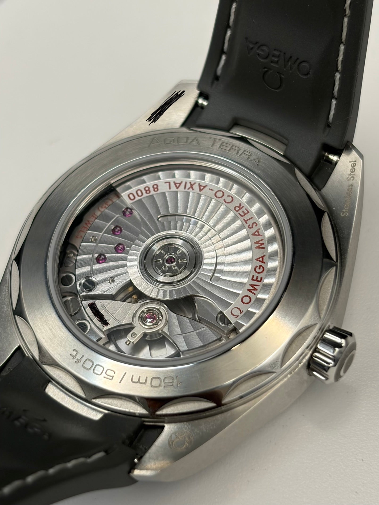 Close-up of the back of an Omega Terra watch with a silver stainless steel case and a black leather strap, showing the detailed automatic movement through a transparent case back.