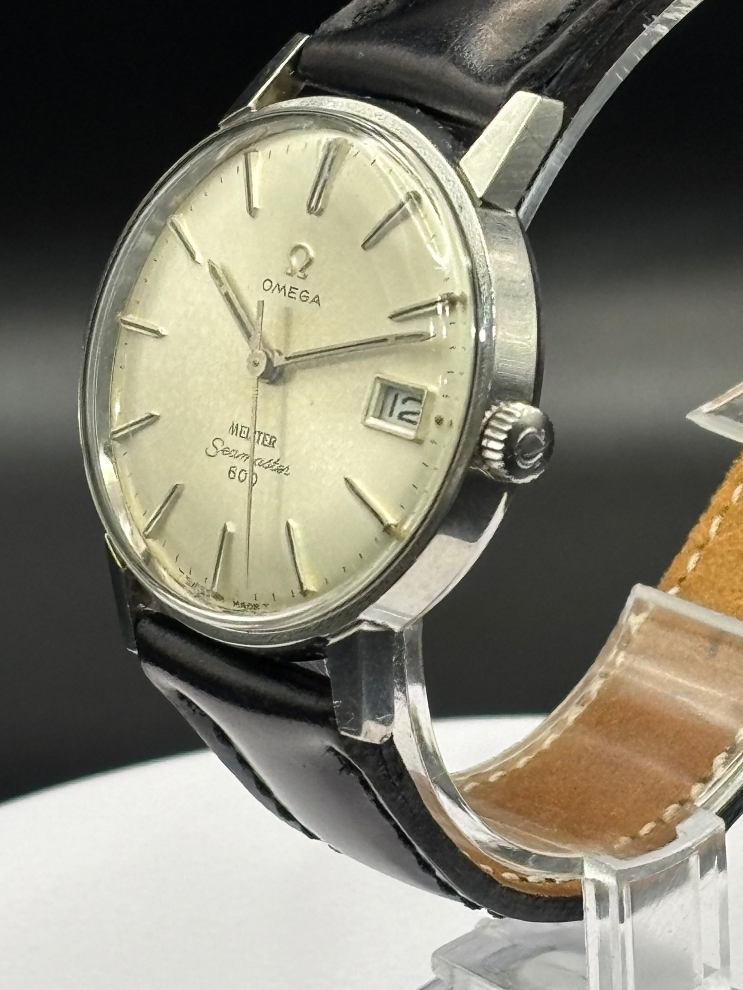 Vintage Omega watch with black leather strap on a clear stand against a dark background