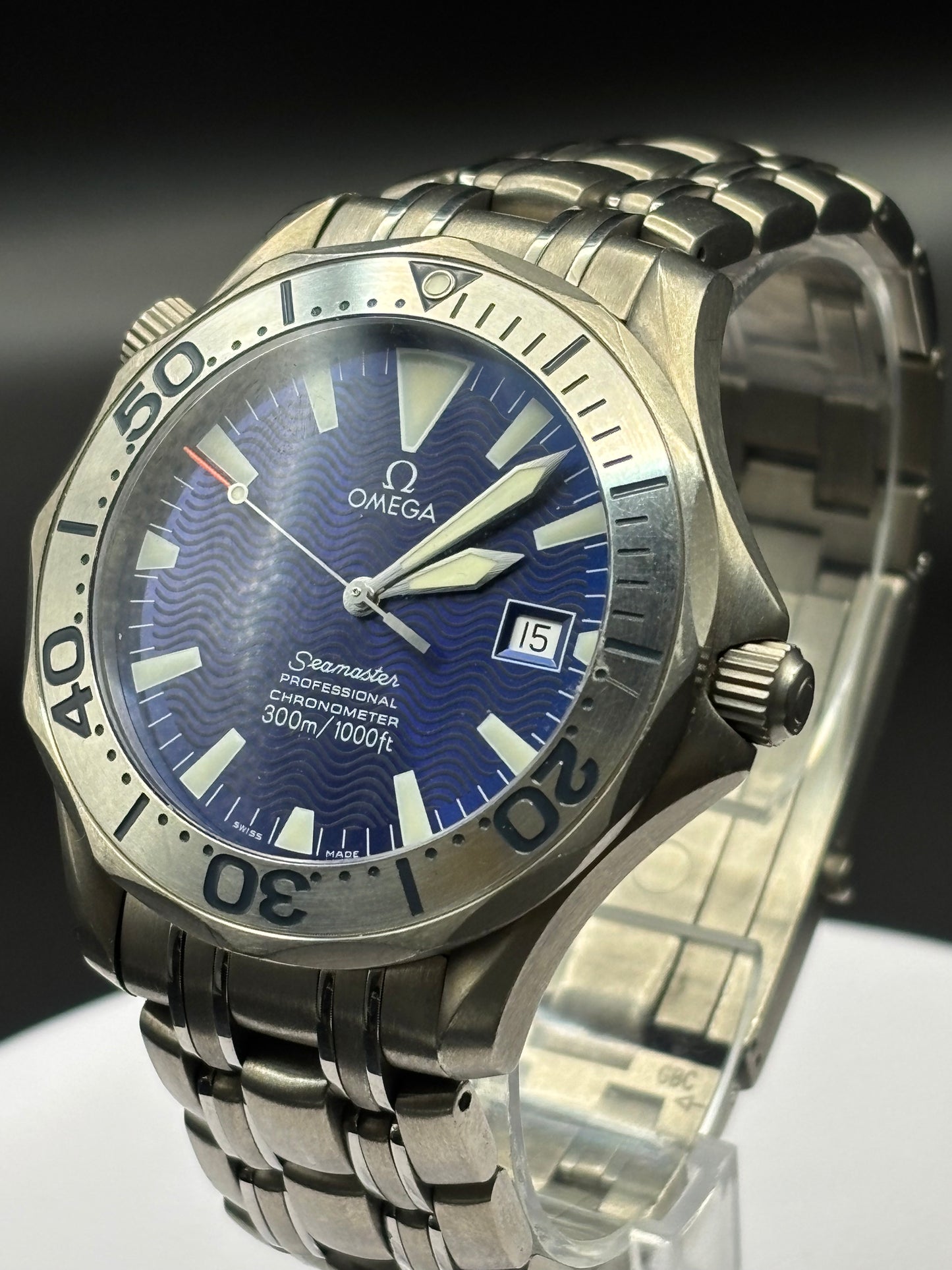 Silver Omega watch with blue dial on a clear stand against a dark background