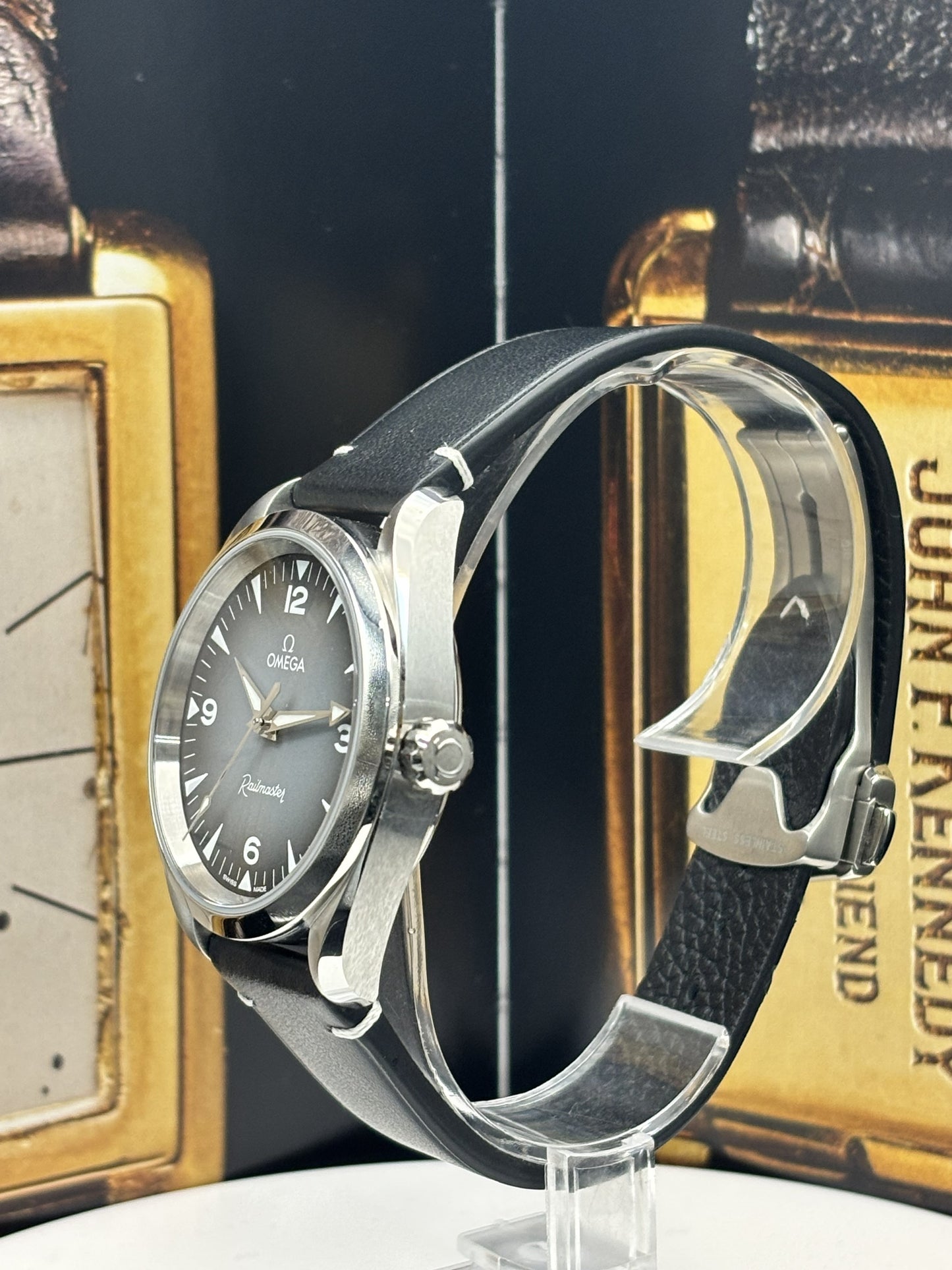 Omega watch with black leather strap on a stand against a vintage book background