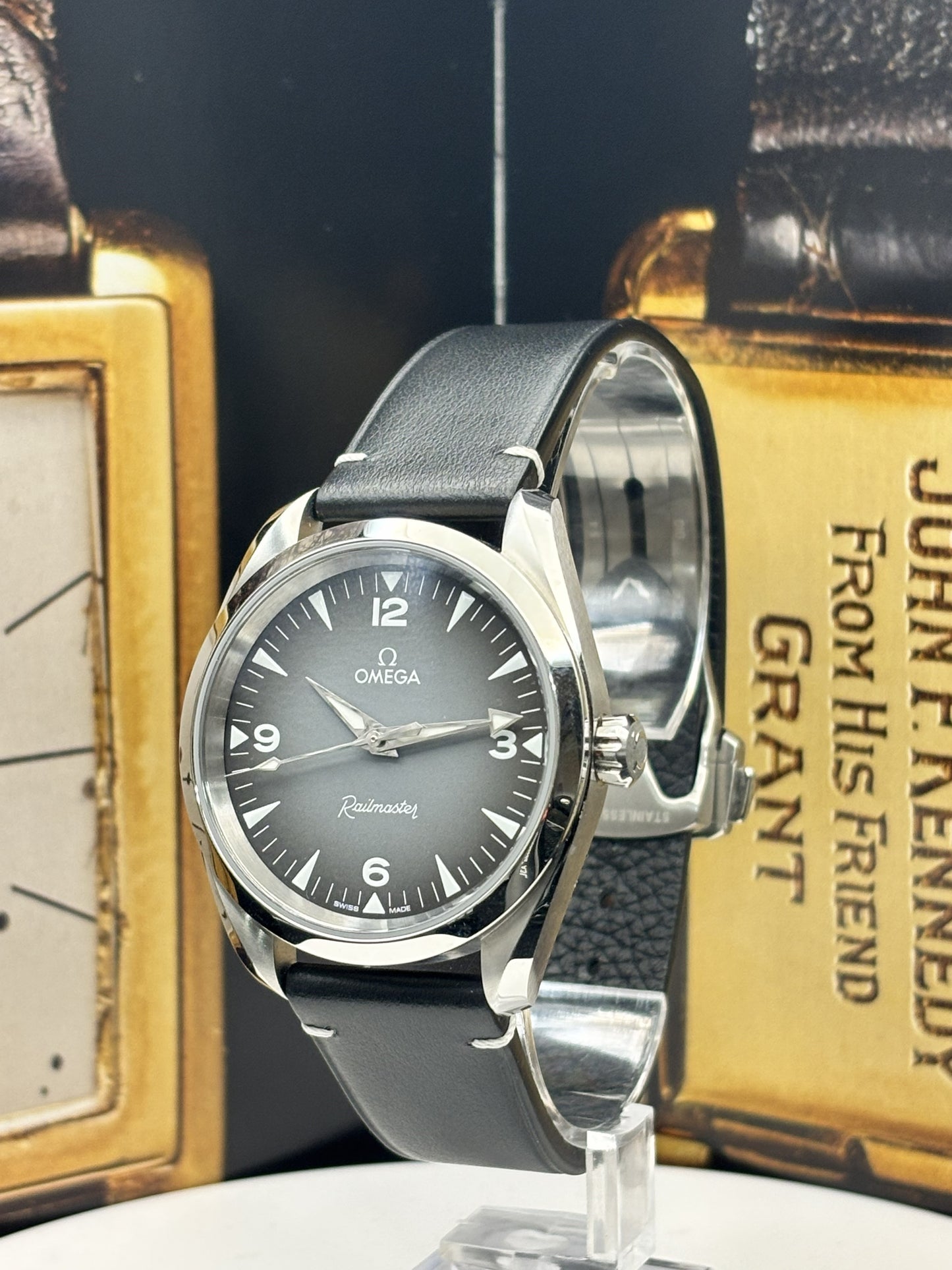 Omega watch with black leather strap on a stand against a vintage book background