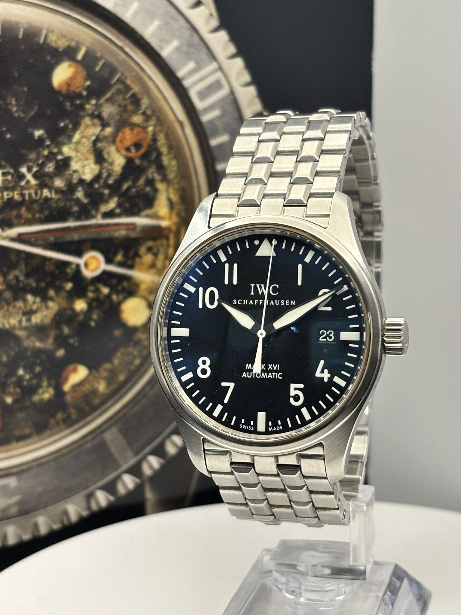 IWC watch with a detailed face and metal bracelet on a stand, with another watch in the background.
