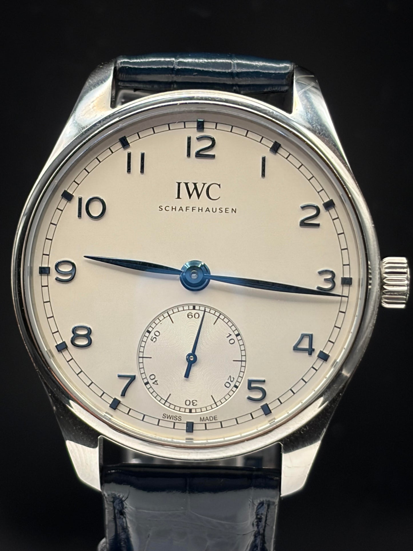 IWC Schaffhausen wristwatch with a silver-toned stainless steel case, cream-colored dial, blue hands and markers, and a dark blue leather strap, shown against a solid black background.