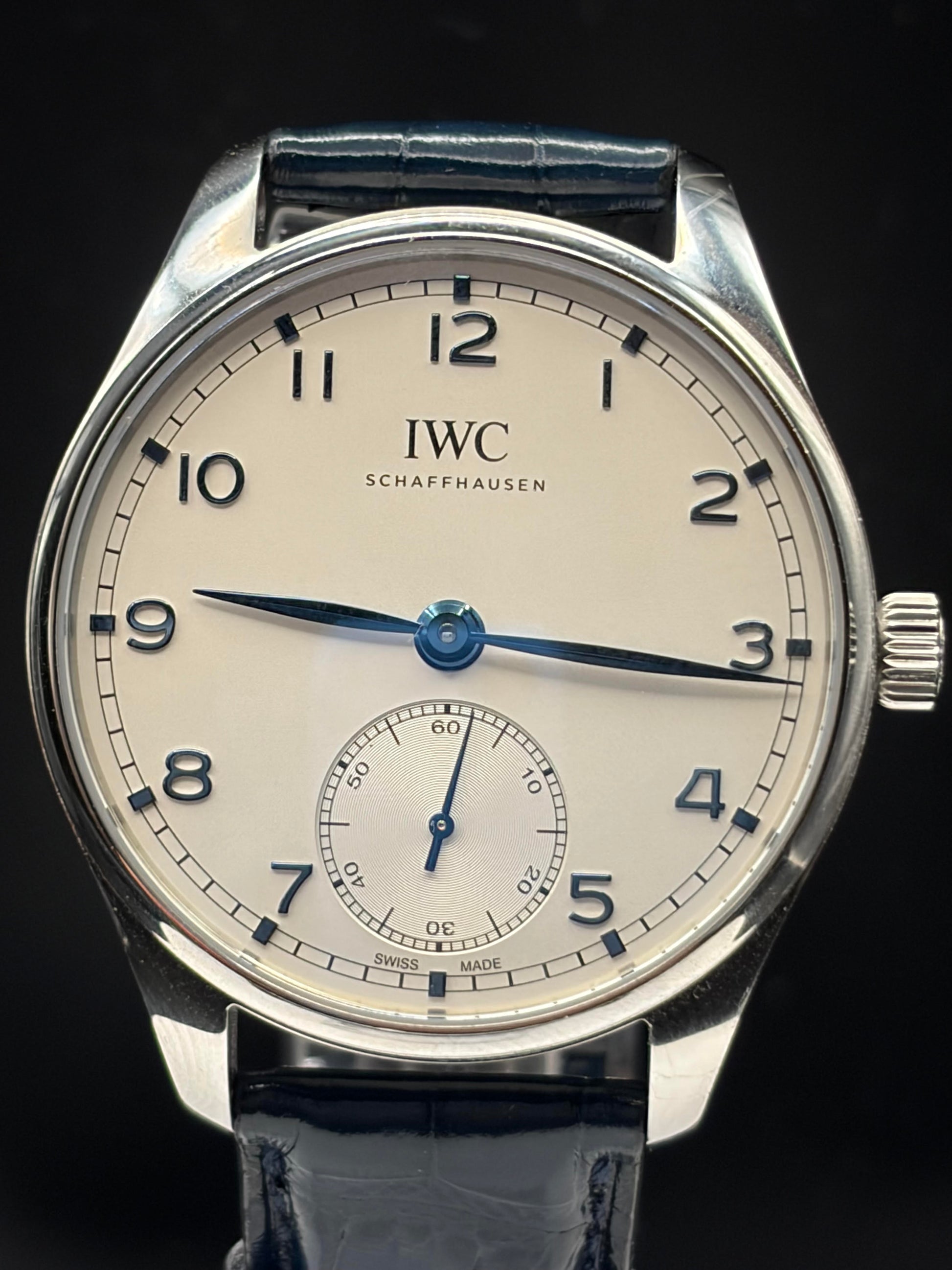 IWC Schaffhausen wristwatch with a silver-toned stainless steel case, cream-colored dial, blue hands and markers, and a dark blue leather strap, shown against a solid black background.