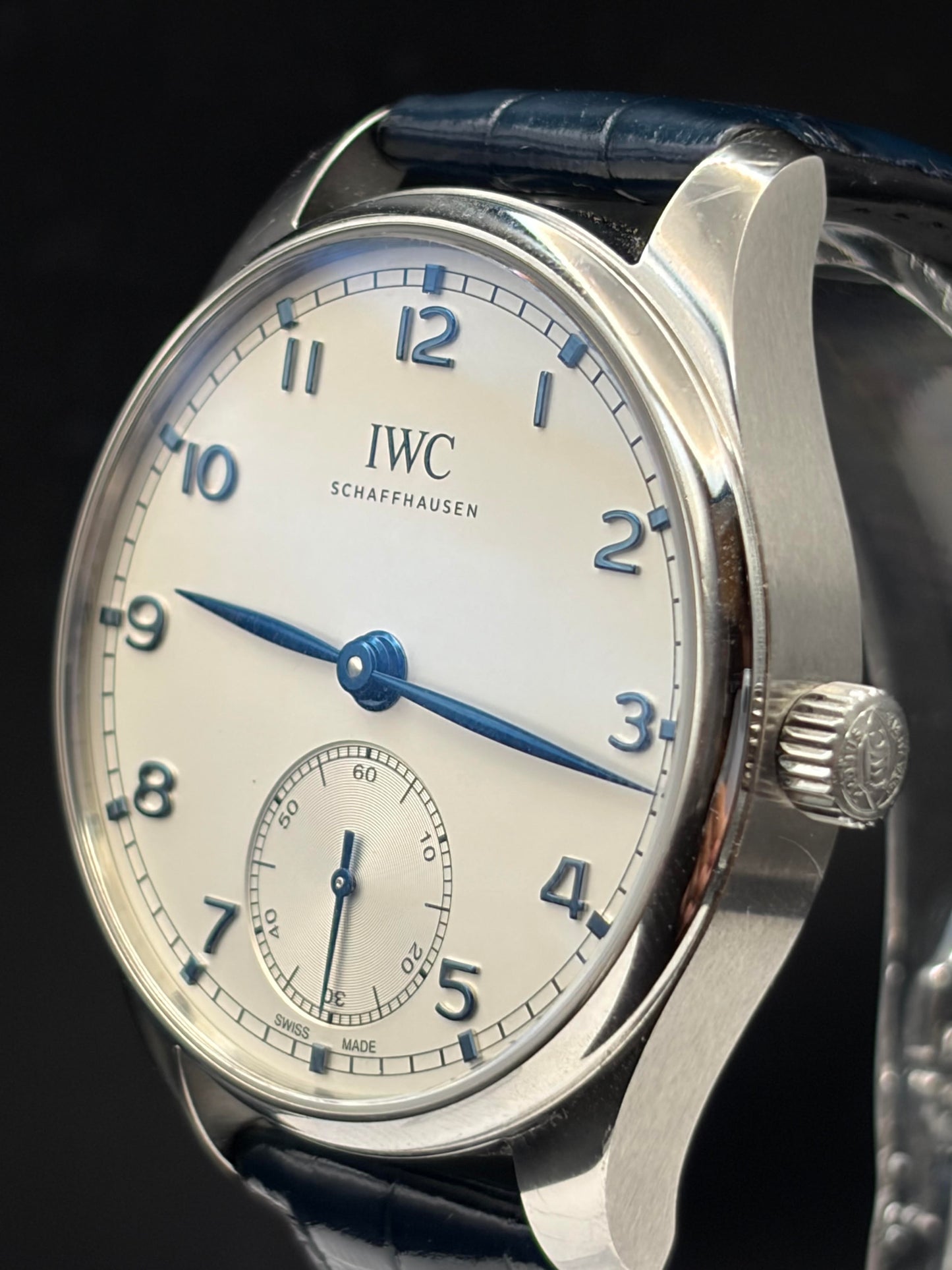 Close-up of an IWC Schaffhausen wristwatch with a silver-toned stainless steel case, white dial, blue numerals and hands, and a dark blue leather strap on a black background.