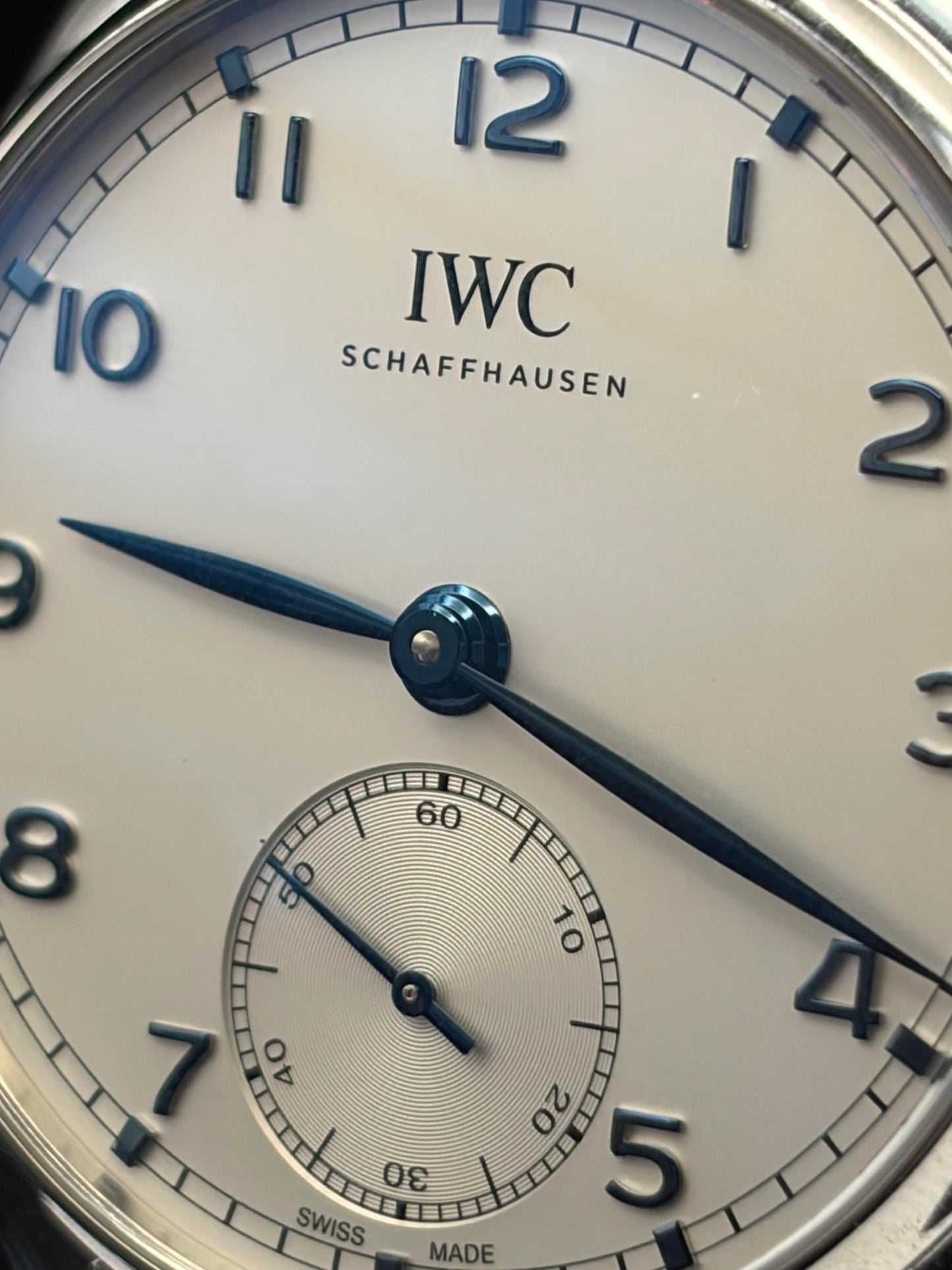 Close-up of an IWC Schaffhausen watch dial showing the white face, black Arabic numerals, blue hands, and a small seconds subdial.