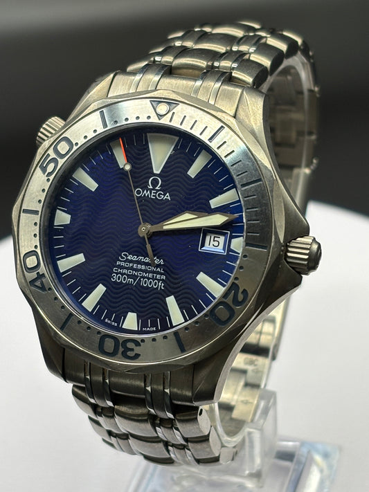 Omega watch with blue dial and metal band on a clear stand against a dark background
