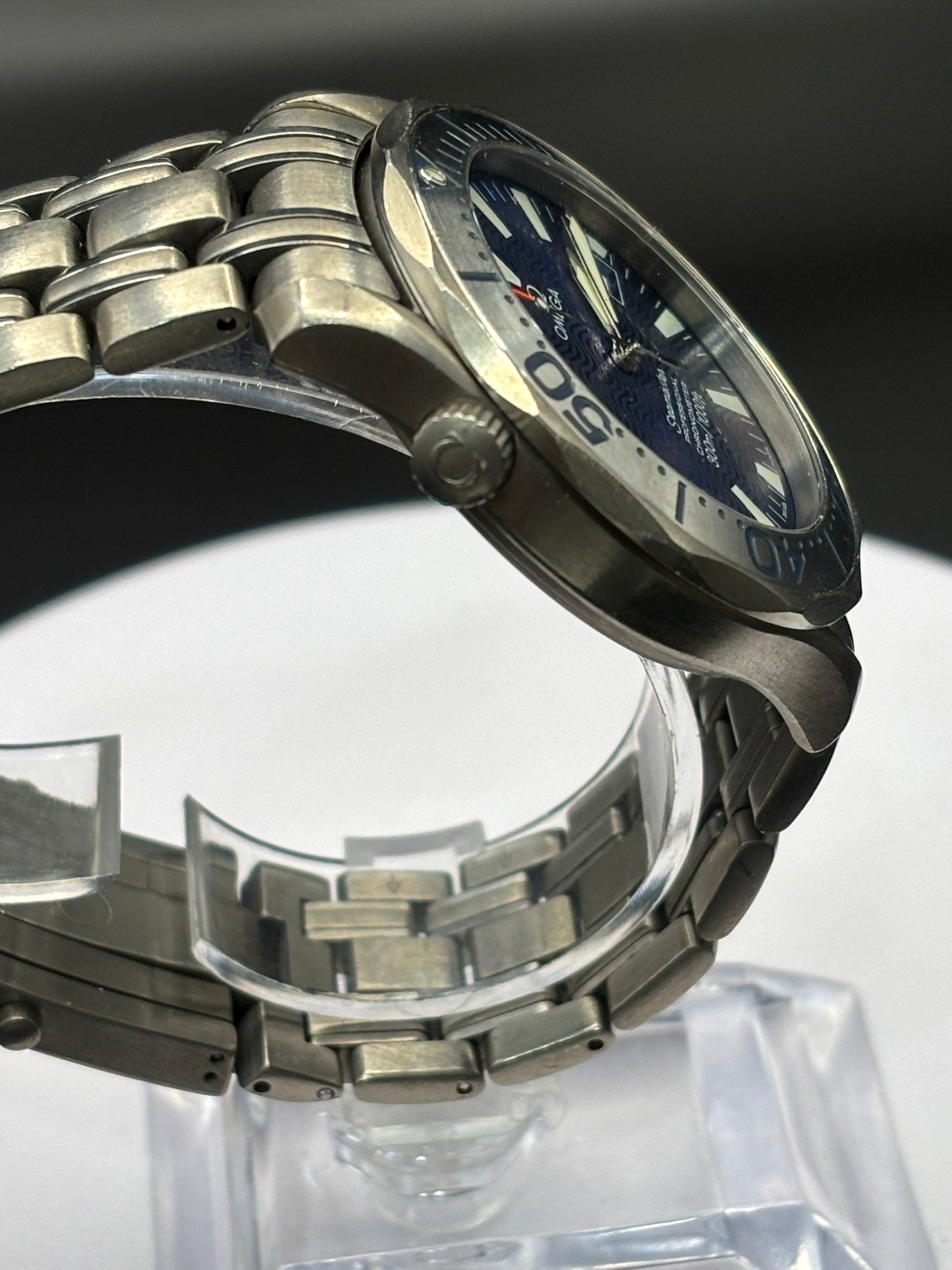 Silver watch with blue face on a clear stand against a dark background