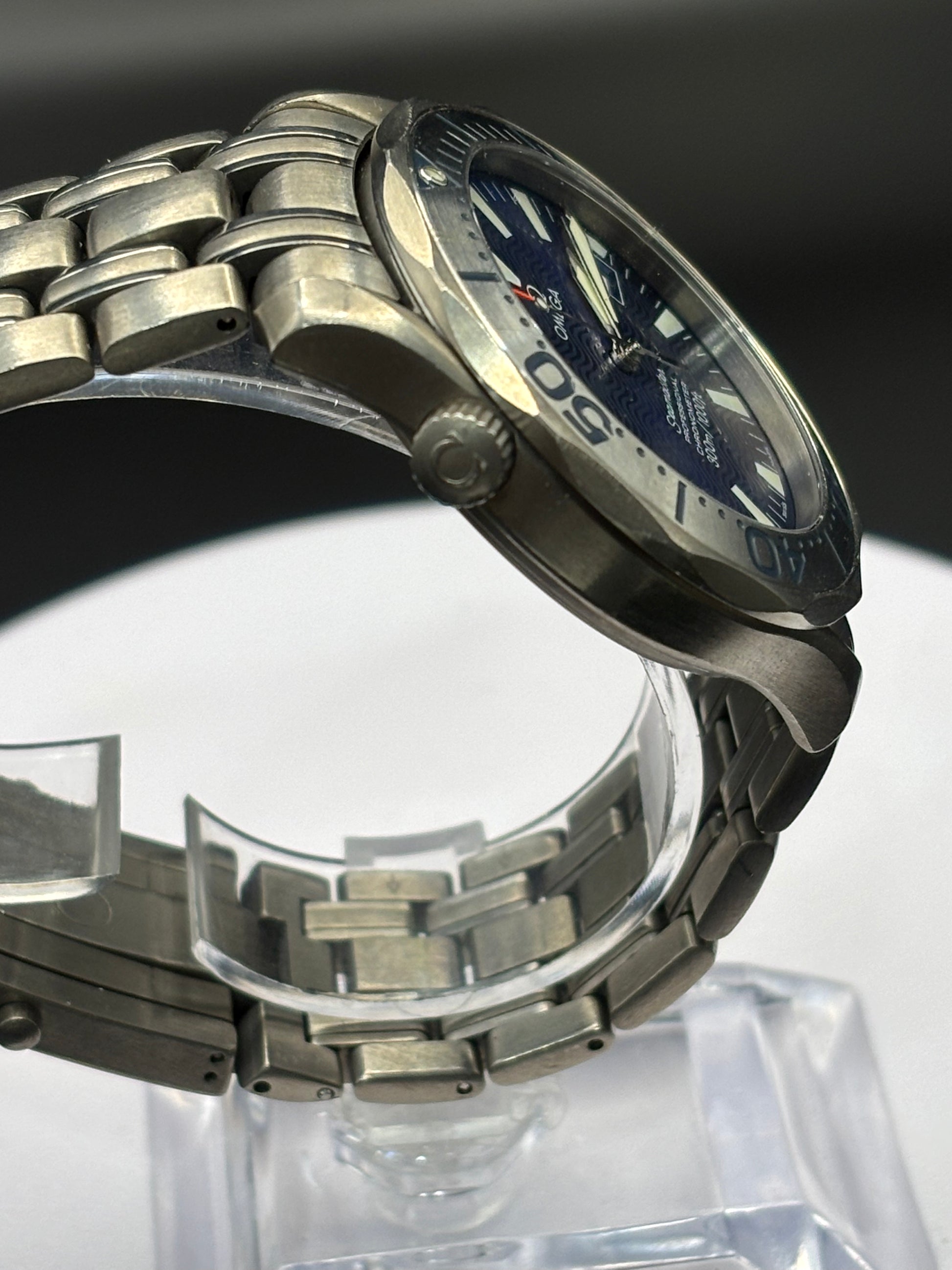 Silver watch with blue face on a clear stand against a dark background