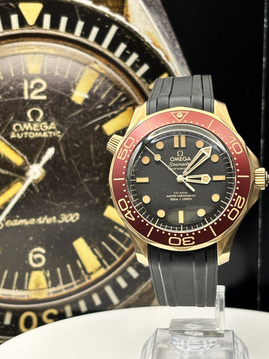 Omega watch with black and red face and gold accents, displayed on a stand with another Omega watch in the background.