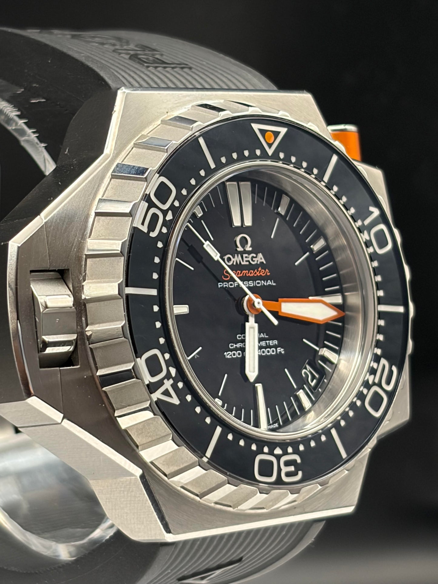 Close-up of an Omega Professional Submariner watch with a silver octagonal case, black dial, black rotating bezel, and orange accents.