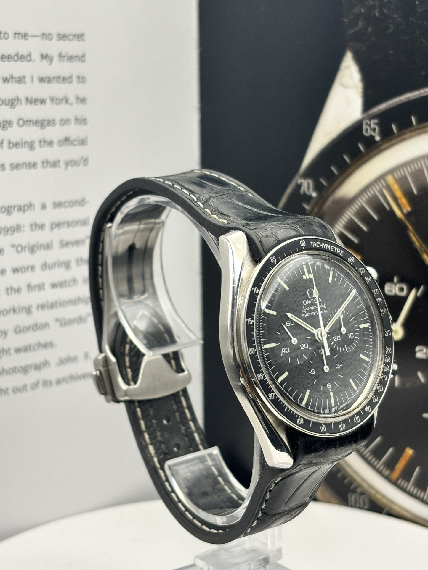 Luxury watch with black strap on a stand, book in the background