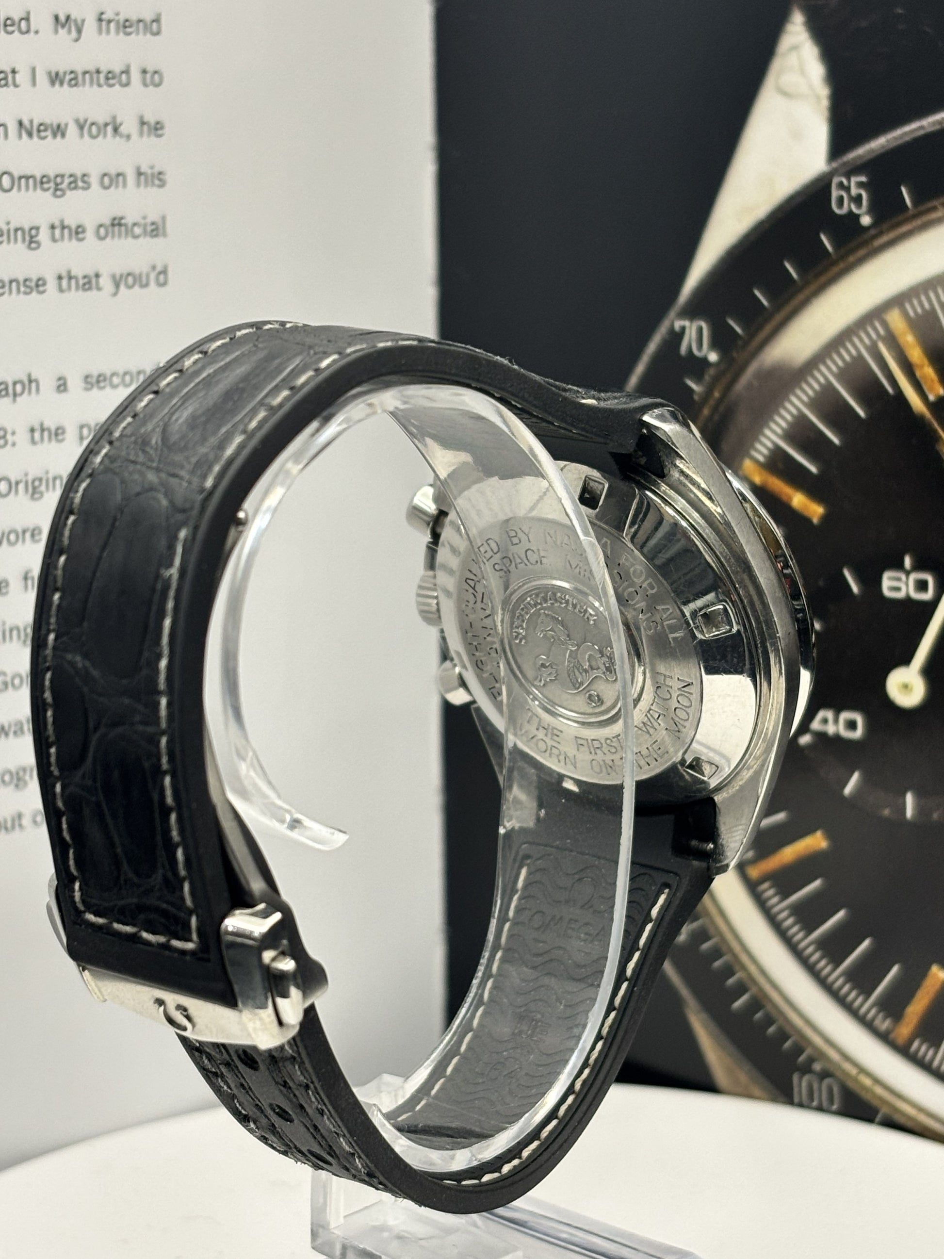 Close-up of a black leather-wrapped watch with a clear face cover on a white surface.