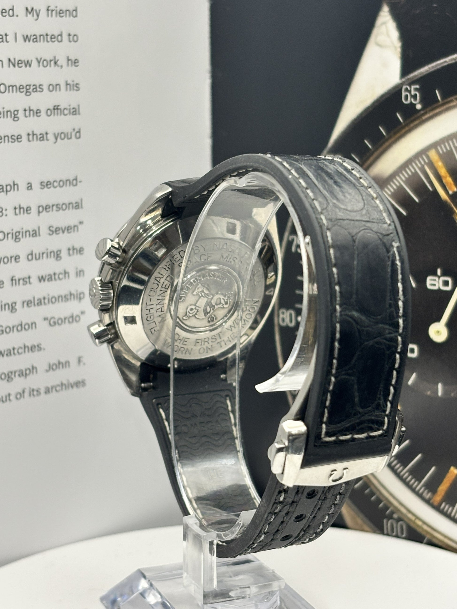 Luxury watch with black leather strap on a stand, with another watch in the background.