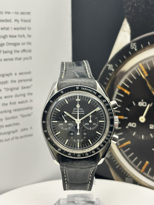 Black wristwatch with detailed face on a white surface, with another watch in the background.
