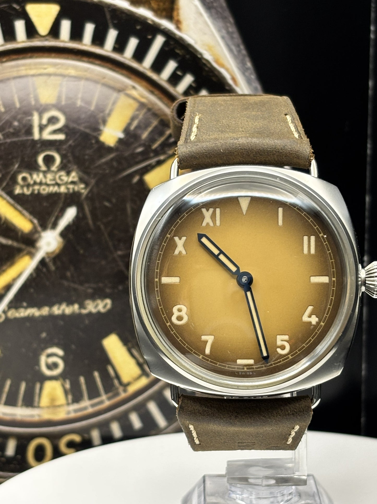 Two vintage watches, one with a brown face and leather strap, the other with a black face and gold accents, on a dark background.