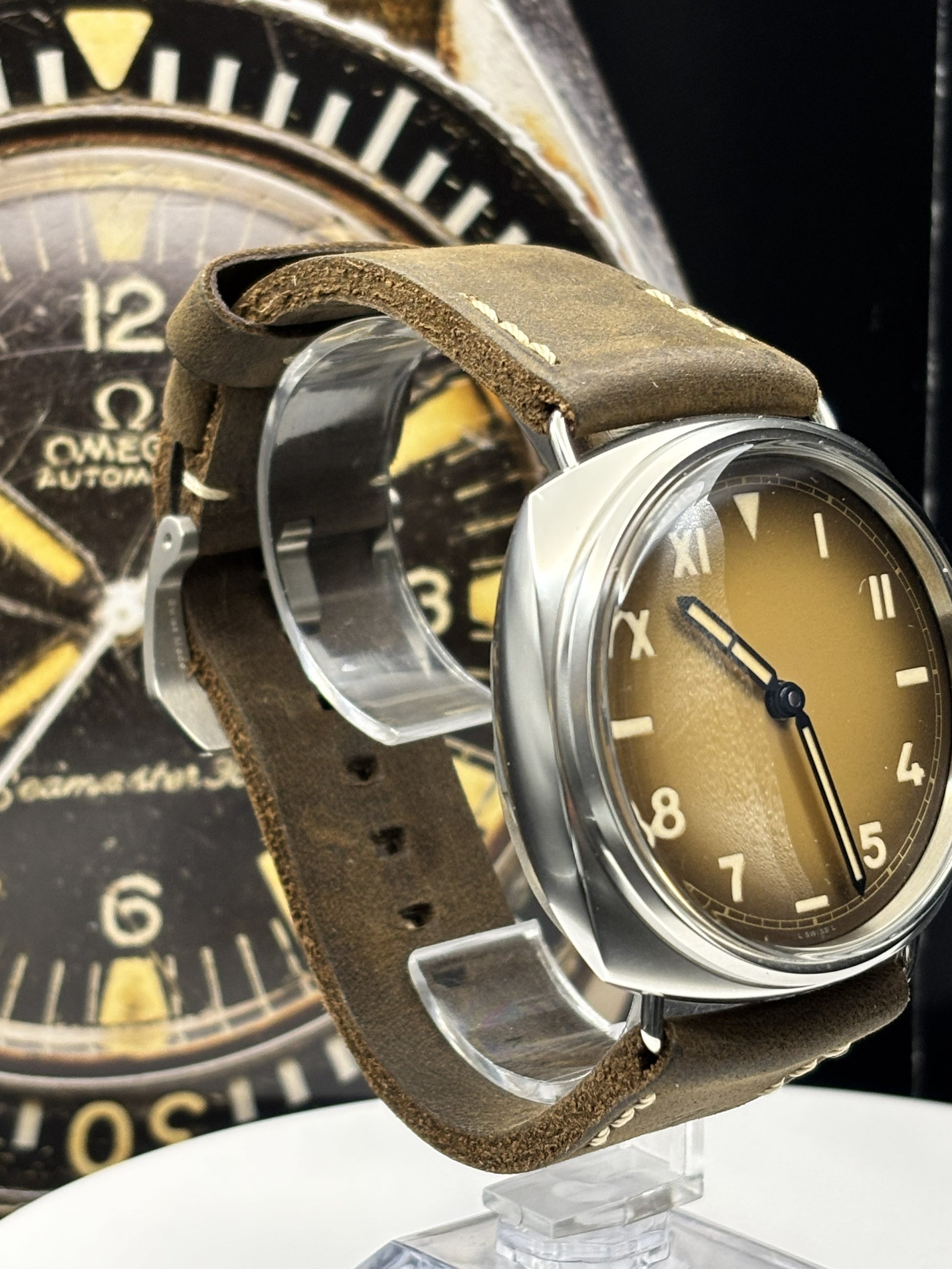 Close-up of a vintage watch with a brown leather strap and gold-dial face, with another watch in the background.