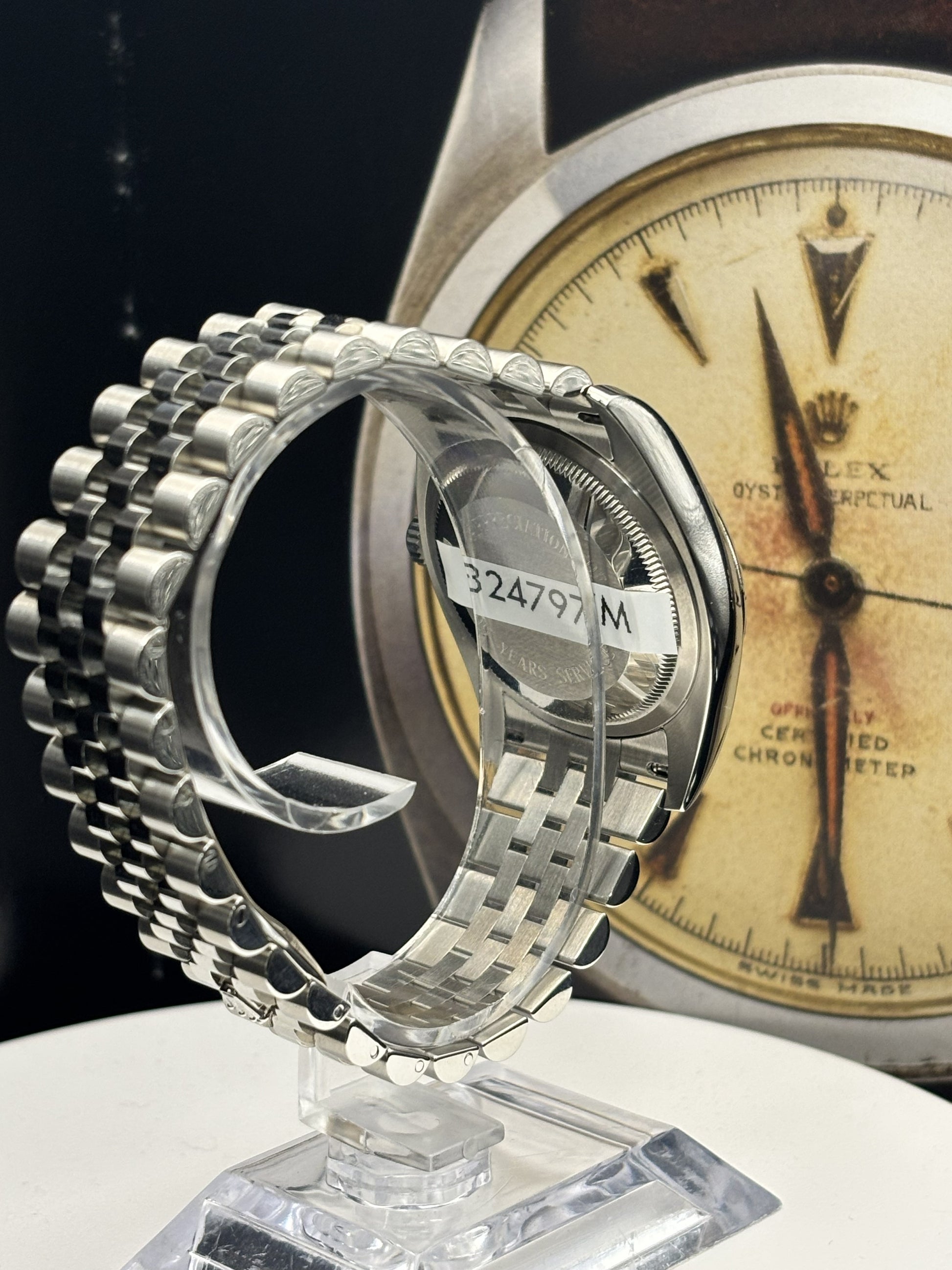 Close-up of a silver watch band on a stand with a vintage-style watch face in the background.