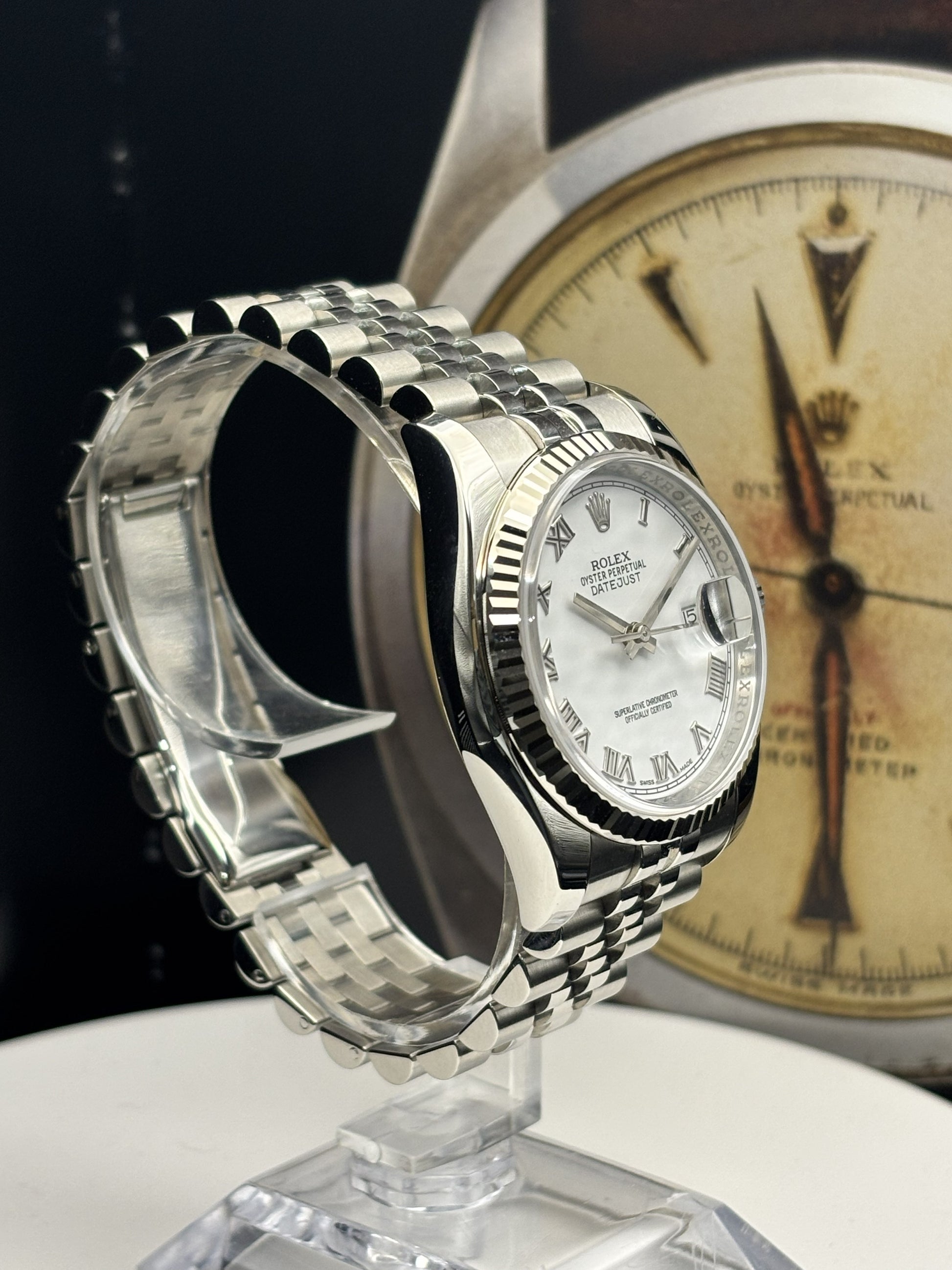 Silver watch on a stand with a blurred vintage Rolex watch in the background