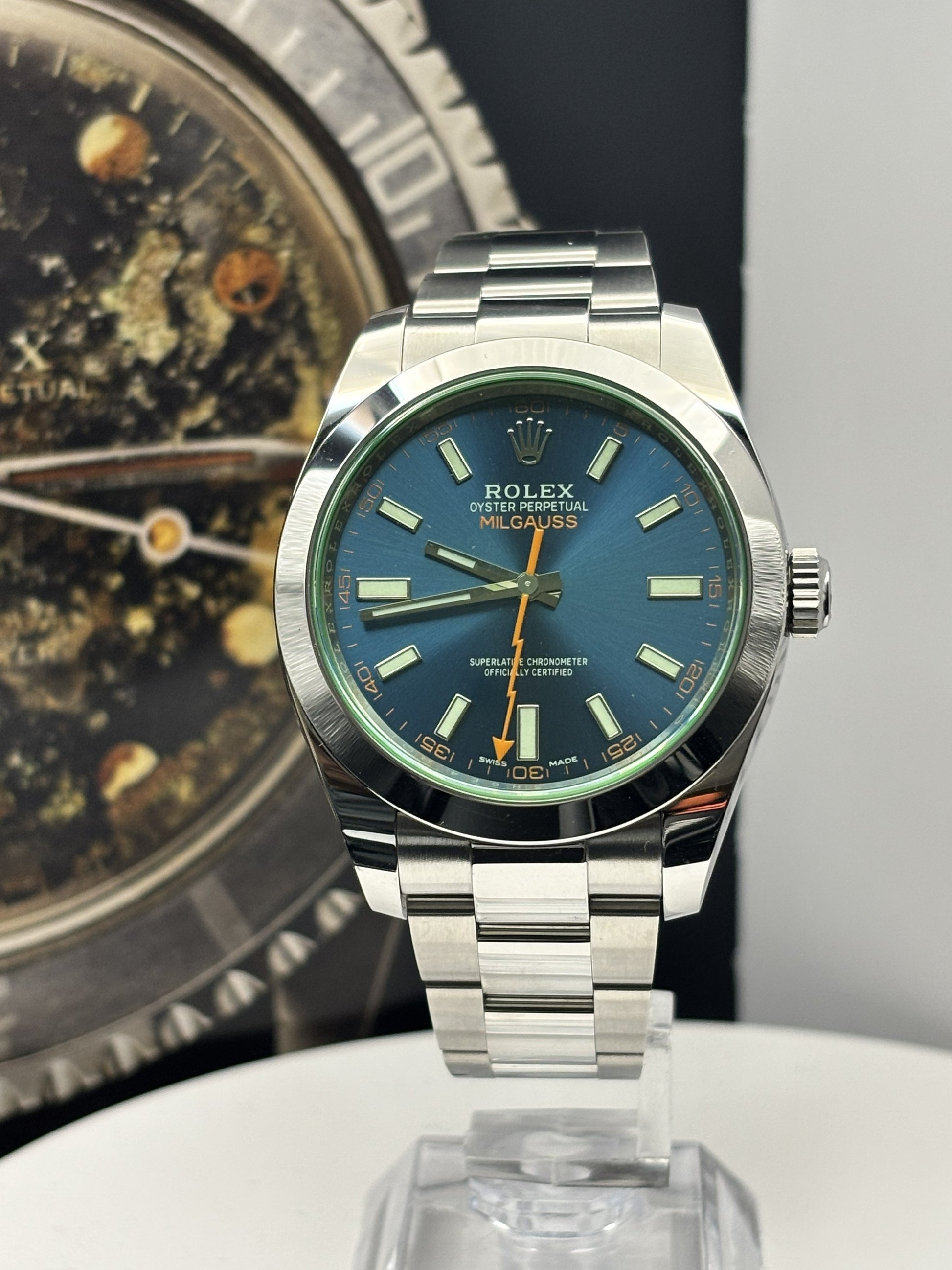 Silver watch with blue face on a reflective surface, with another watch in the background.