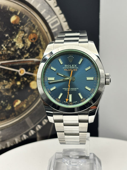 Silver watch with blue face on a reflective surface, with another watch in the background.