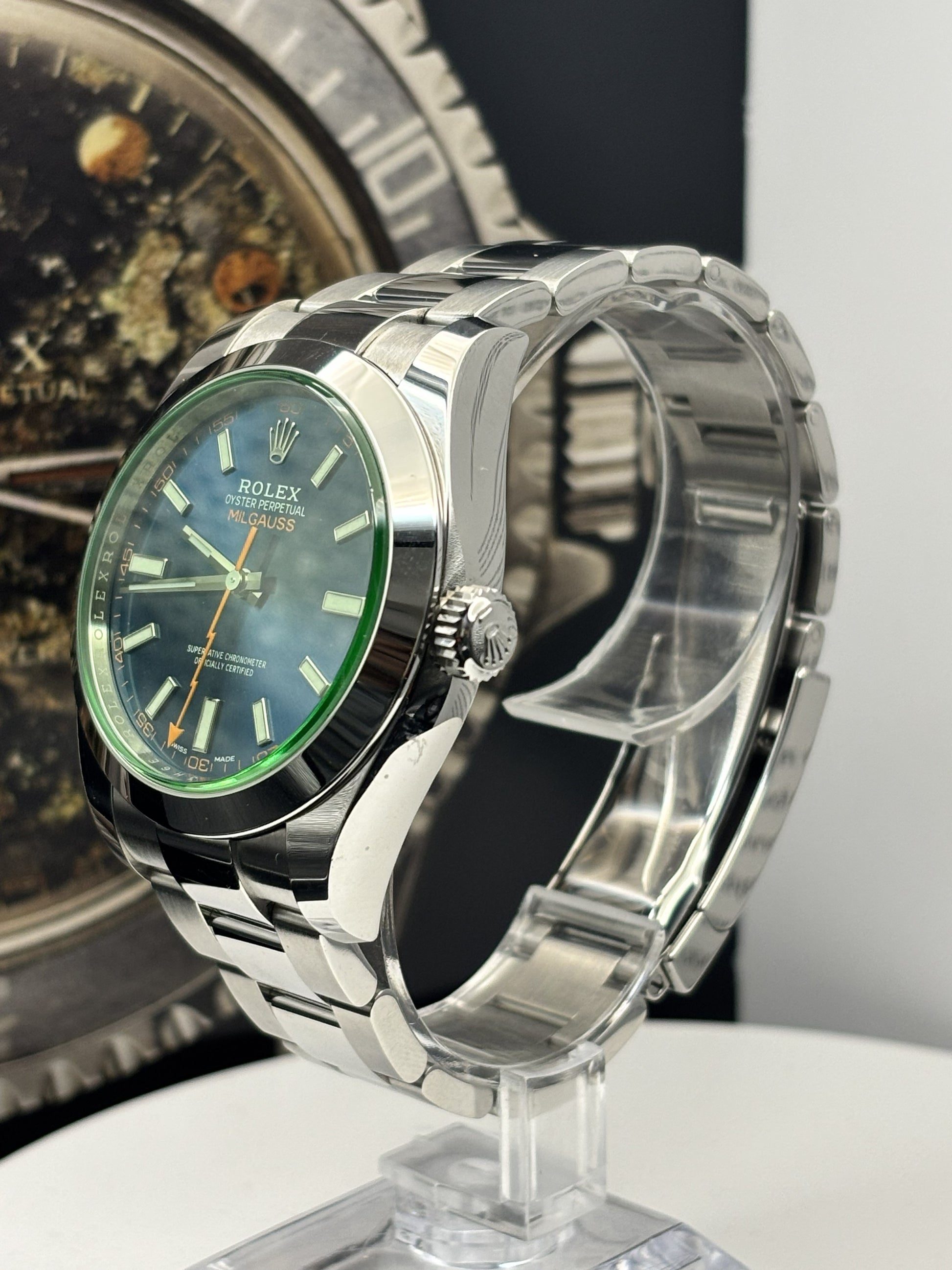 Silver watch with green face on a stand against a dark background