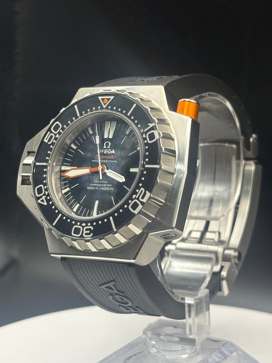 Omega x Swatch Submariner Date watch with a silver-toned octagonal case, black dial, black bezel, and black rubber strap, displayed on a clear stand against a dark background.
