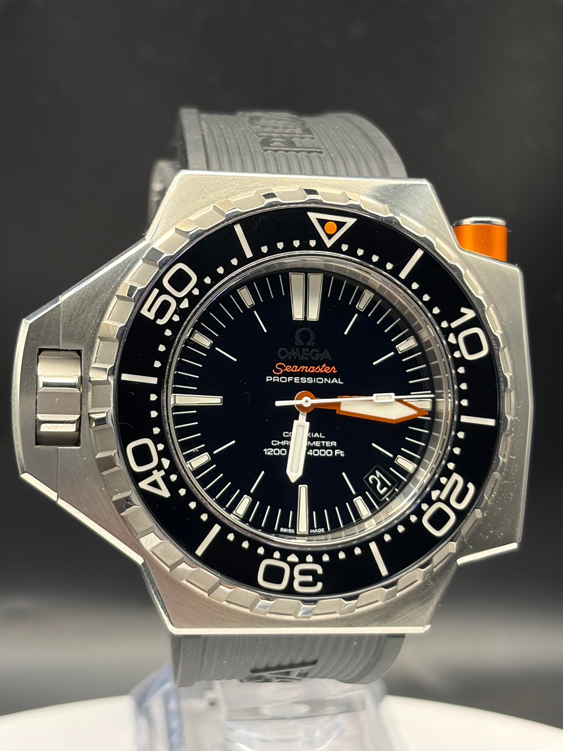 Omega Seamaster Professional diver watch with a silver stainless steel case, black dial, black rotating bezel, and orange accents, shown on a clear display stand against a dark background.