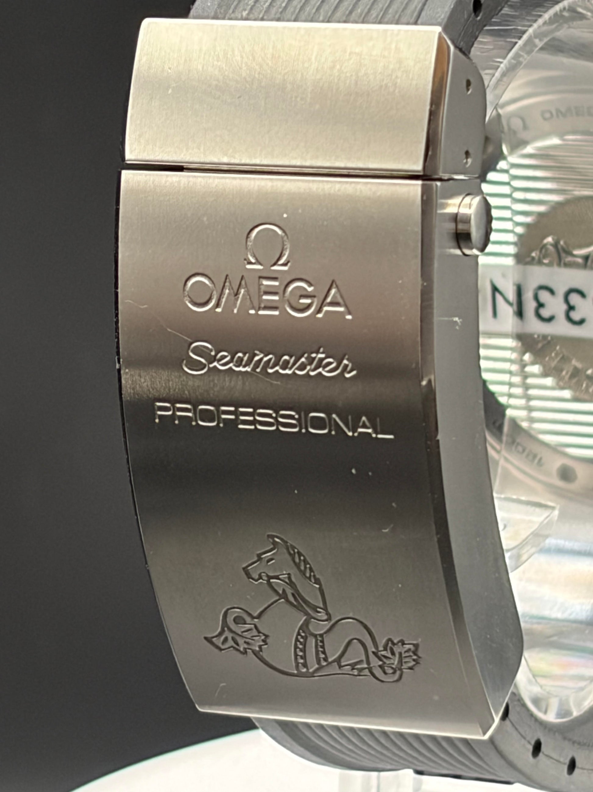 Close-up of an Omega Seamaster Professional watch clasp showing the brushed stainless steel metal with engraved branding and a horse-and-anchor logo.